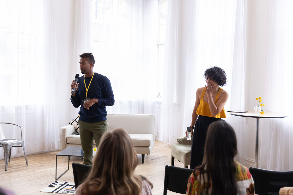 Andre Essue holding a microphone mid-sentence while a participant standing nearby reacts.